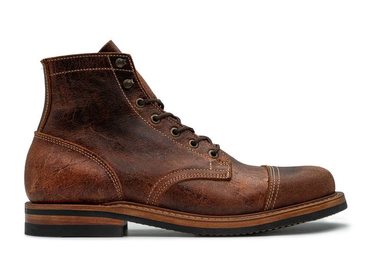 side view of brown textured leather boot on white background