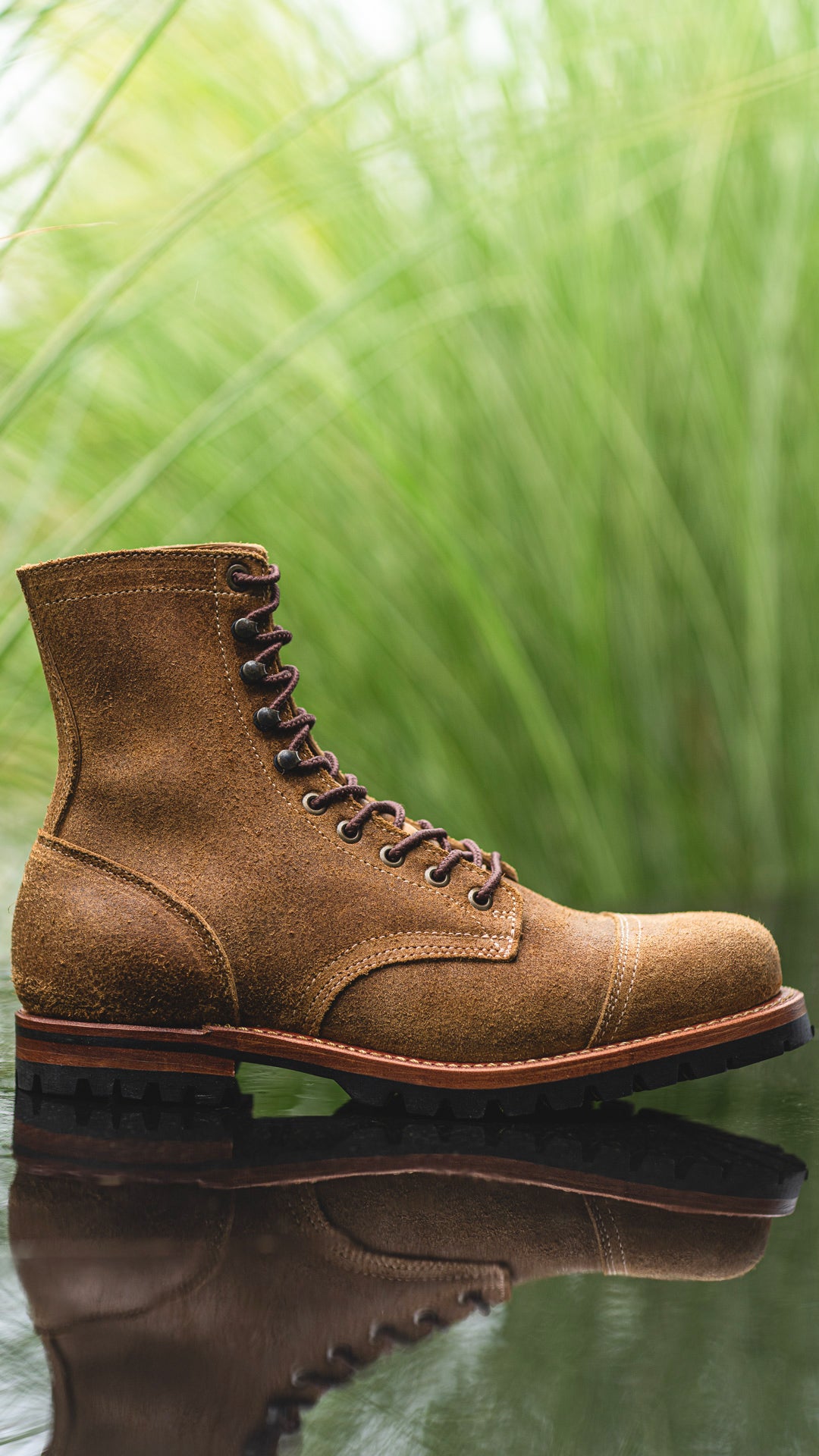 side view of coyote oiled rough out upland boot with shallow depth of focus against out of focus greenery