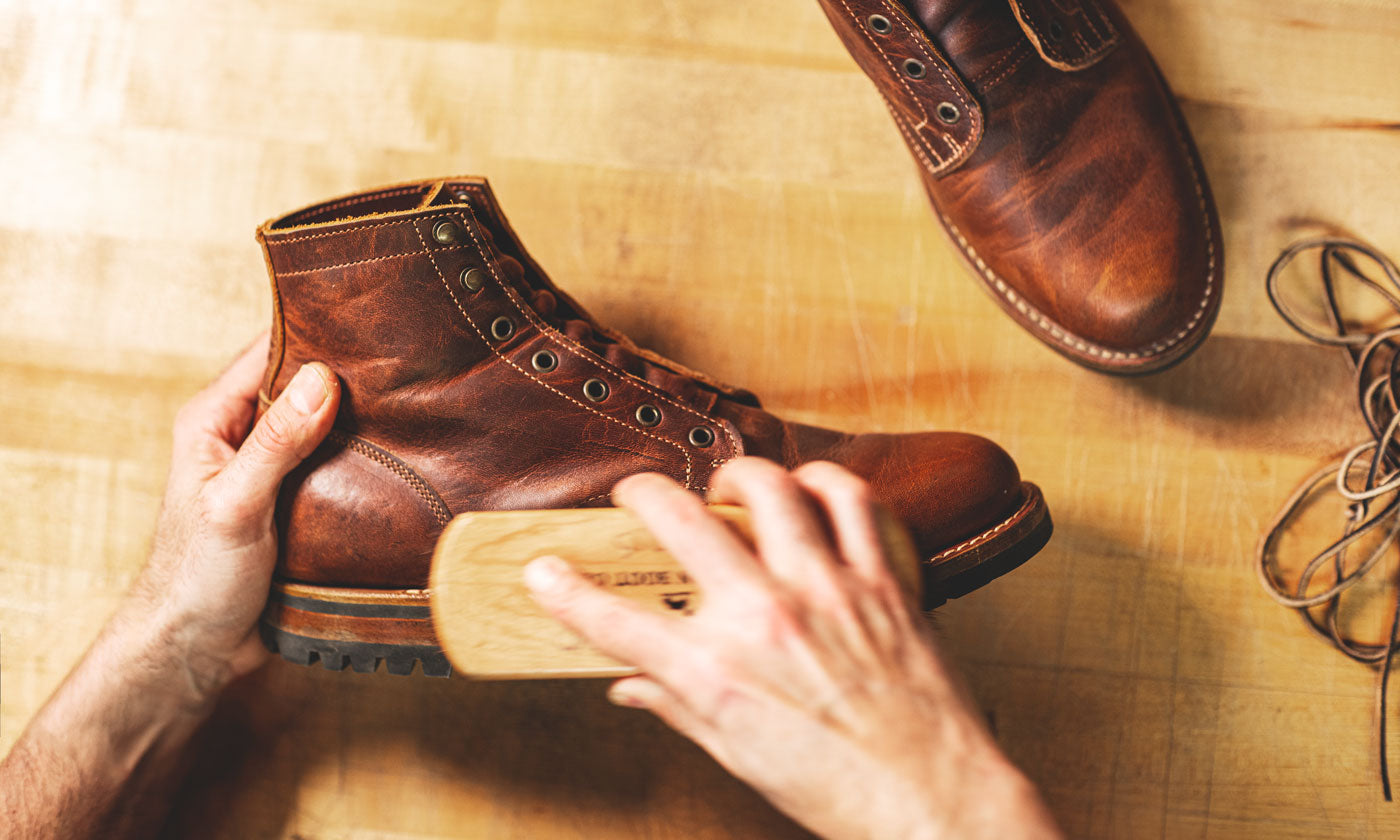 man cleaning leather boot with horsehair brush