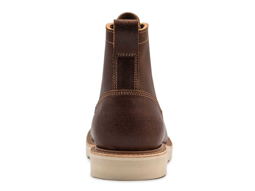 Brown leather moc toe boot with yellow laces on a white background view from behind