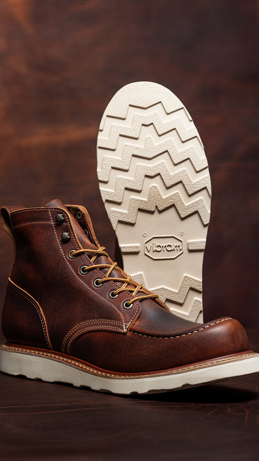 rustic tobacco snakebite leather moc toe boots on brown leather backdrop